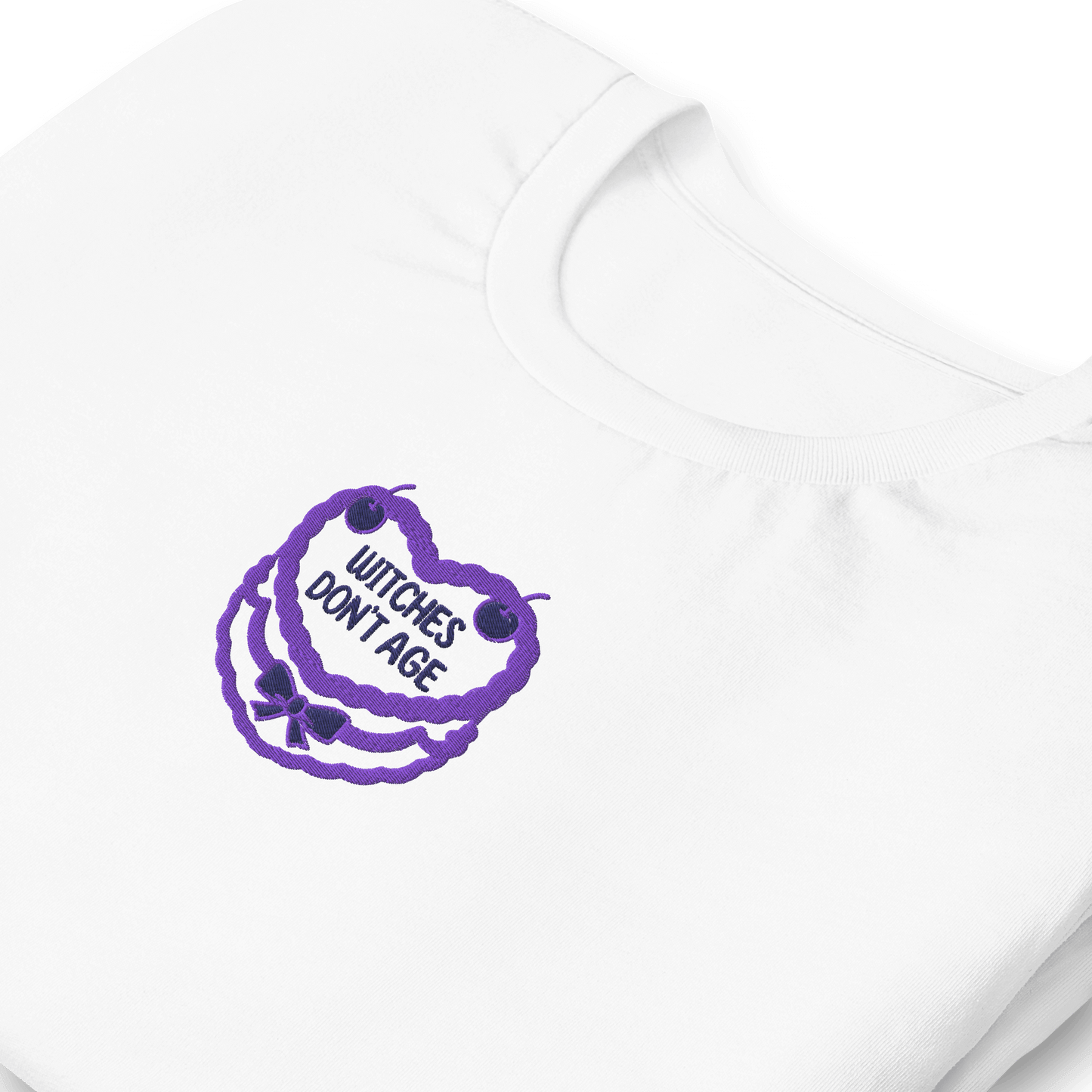 Maglietta bianca con ricamo 'Witches don't age' in viola, ideale per compleanni con stile e ironia.