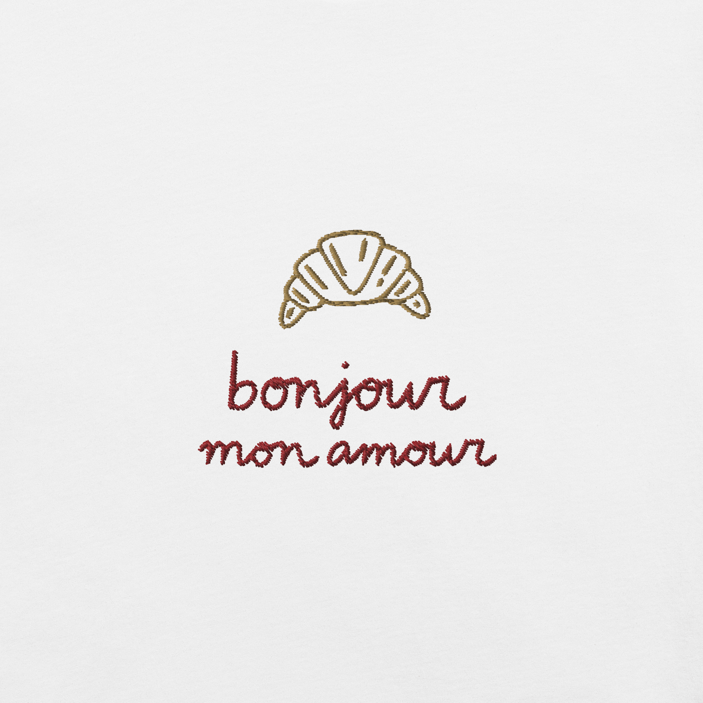 Ricamo di croissant con la scritta 'bonjour mon amour' su maglietta bianca, dettagli romantici ed eleganti.