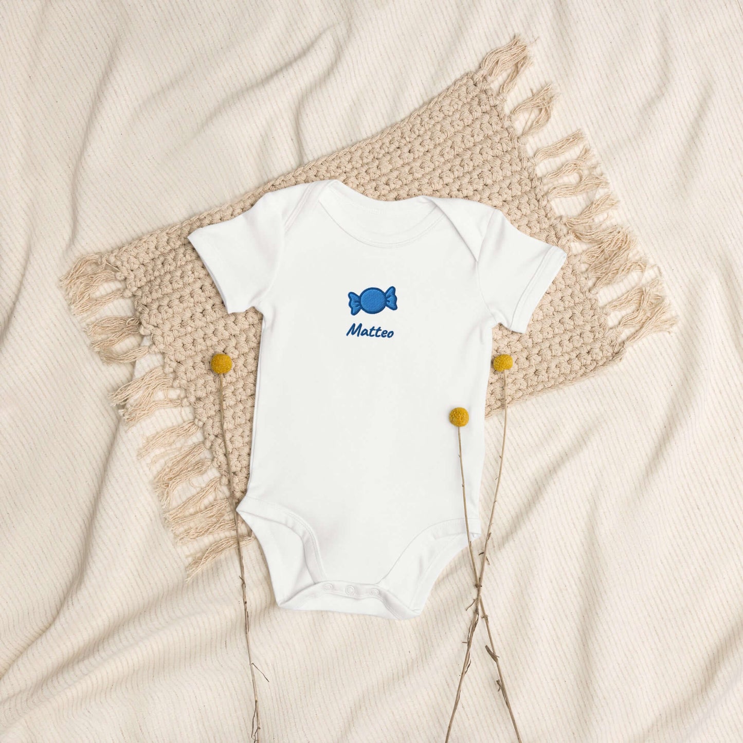 Body neonato bianco "Candy Crushin" in cotone organico con ricamo blu su sfondo neutro.
