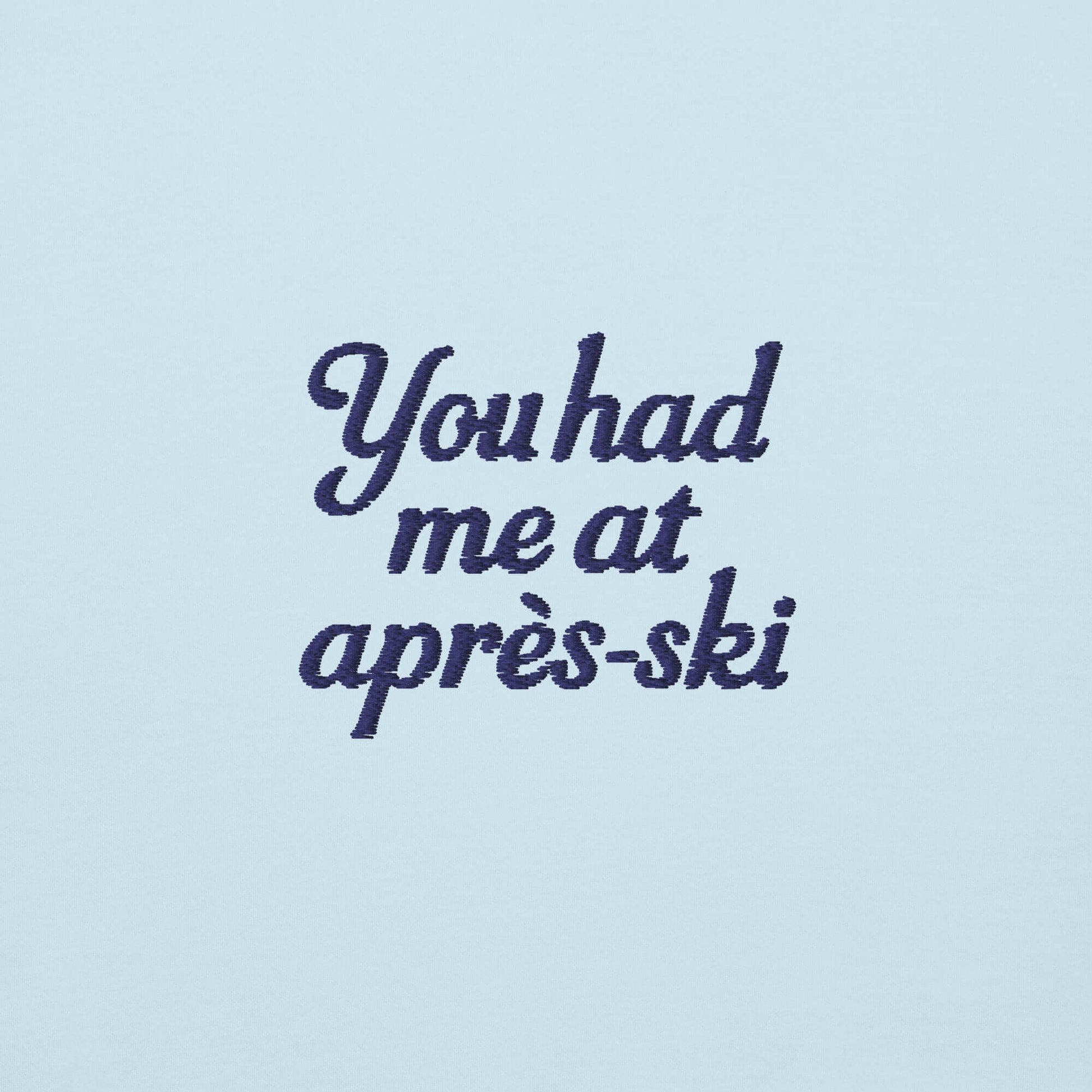 Scritta ricamata su felpa azzurra: "You had me at après-ski" in stile elegante e divertente.