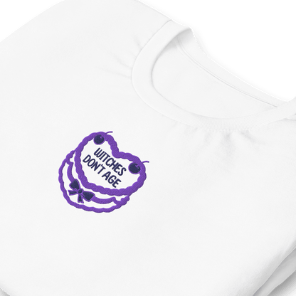 Maglietta bianca con ricamo 'Witches don't age' in viola, ideale per compleanni con stile e ironia.