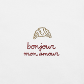 Ricamo di croissant con la scritta 'bonjour mon amour' su maglietta bianca, dettagli romantici ed eleganti.