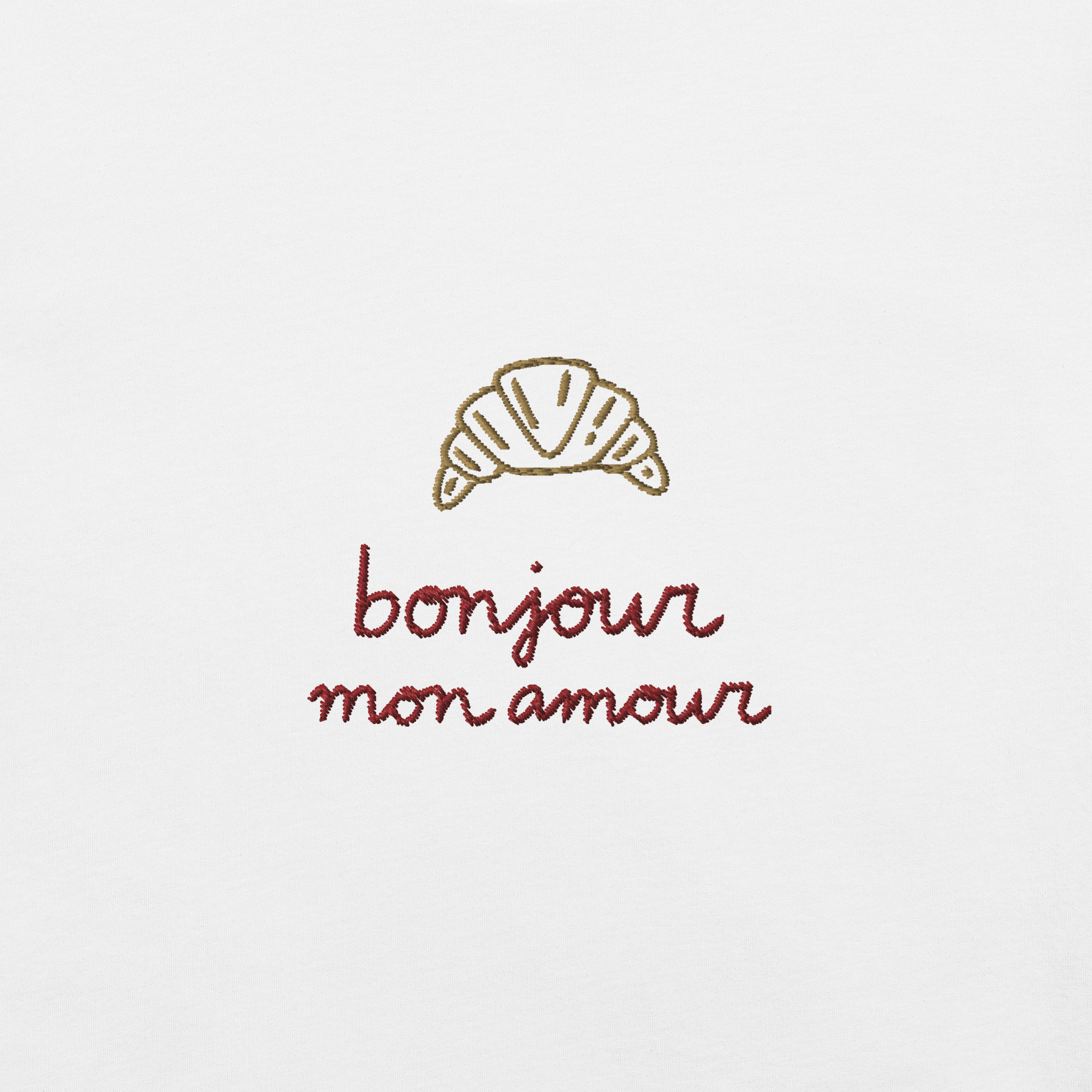 Ricamo di croissant con la scritta 'bonjour mon amour' su maglietta bianca, dettagli romantici ed eleganti.