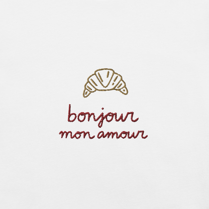 Ricamo di croissant con la scritta 'bonjour mon amour' su maglietta bianca, dettagli romantici ed eleganti.