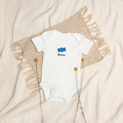 Body neonato bianco "Candy Crushin" in cotone organico con ricamo blu su sfondo neutro.